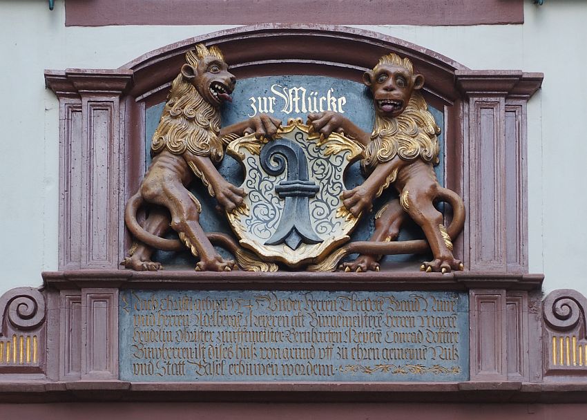 The two lions hold a shield between them. They both stick out their tongues, one looking at the other, and one looking toward the camera. 