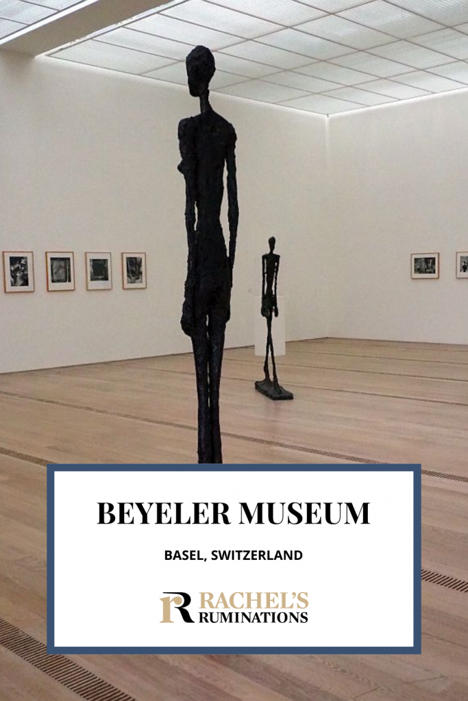 Text: Beyeler Museum, Basel, Switzerland. Image: A Giacometti standing figure with another Giacometti figure in the background.