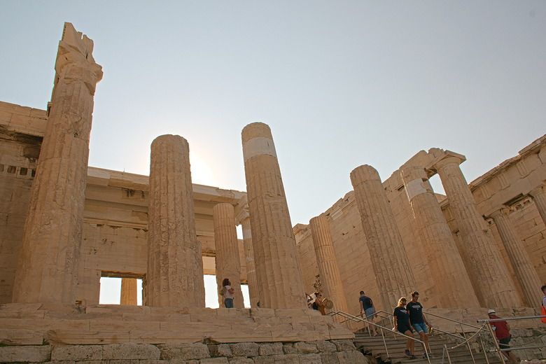 A modern stairway at the bottom left of the photo has a few people on it. Rising above them are huge columns, though the tops are missing from most of them. The columns must have supported a wide portico.