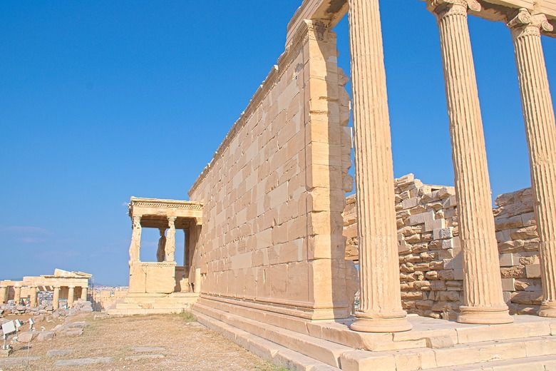 Seen from the corner of the building, the side on the right is a row of columns, holding up a cross piece. The side looknig straight ahead is a wall made of rectangular stones, with a small entrance porch sticking out at the far end: it has statues holding up a small flat roof, not as tall as the wall.