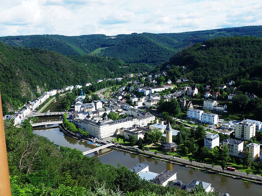 Looking down on Bad Ems, Germany, the river curves out of sight between the surrounding hills. Three bridges cross it. A scattering of buildings along the far bank and behind where the land is fairly flat. On the near side a single row of buildings backed by a steep hill.