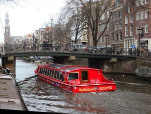 A bright red canal tour boat passes under a bridge.