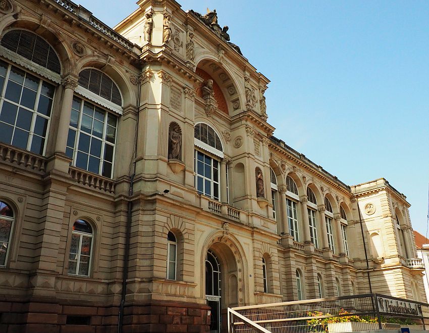 An ornate entrance: arched entry way on the ground floor and large arched windows on the upper story. More arches above those. A bust, presumably of Kaiser Friedrich, above the central entrance, and more statuary in niches and on the roof.