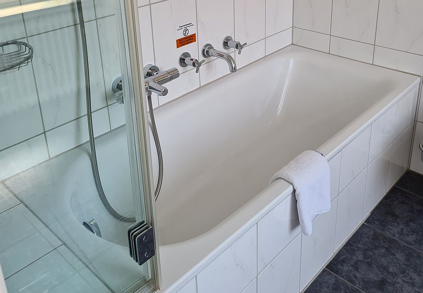 An ordinary white bathtub, but it has two sets of taps: one modern one in a rod shape that has a twisting knob at each end, and one more old-fashioned one, with a faucet in the middle and two separate taps.