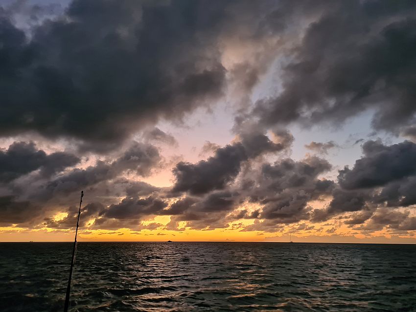 The sun has gone down, but the sky has a lot of distinct fluffy clouds that look quite dark in silhouette against the still lit sky. Near the horizon are gradual shades from orange to yellow.