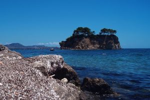 In the foreground a rocky bit of shoreline and the blue water lapping at it. In the background, the island, rising straight out of the water, cliffs on the sides, flat on top with a scattering of trees.