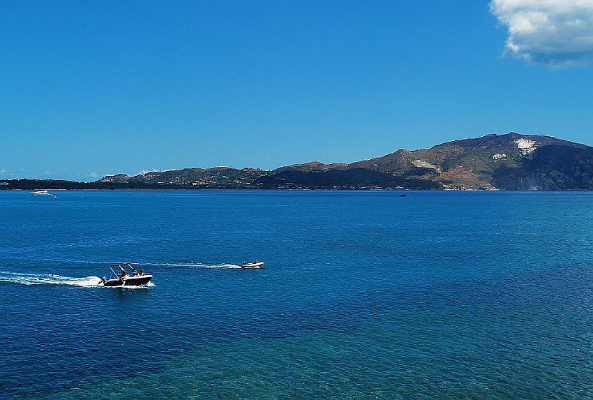 A view over water from Cameo Island Zakynthos. In the distance is another island or perhaps the Pelleponese, with low mountains rising from the sea. In the foreground are two motorboats.