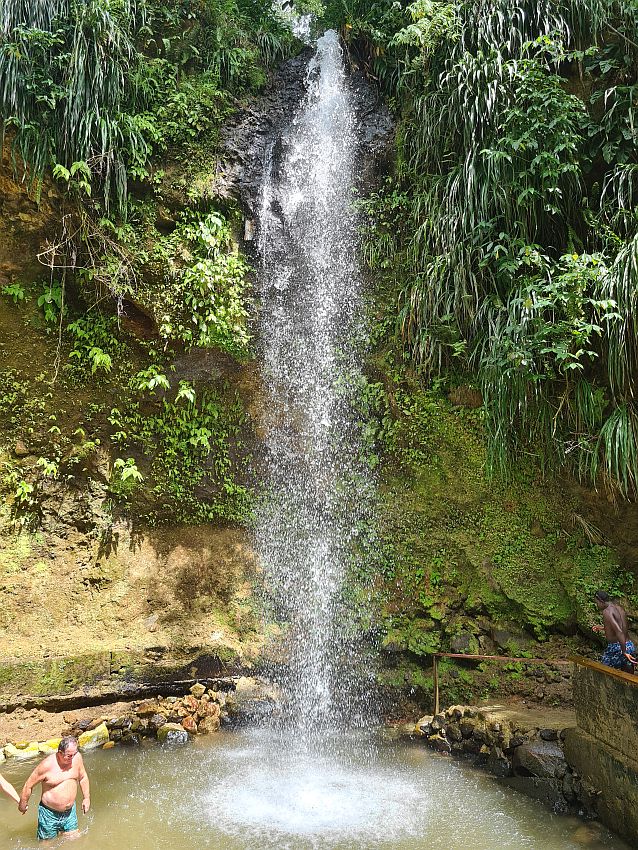 The waterfall is very tall and narrow, splashing down in a round pool after passing a greenery-covered cliff. At the bottom of the photo a man can be seen, showing how high Toraille waterfall is: perhaps 6 stories?