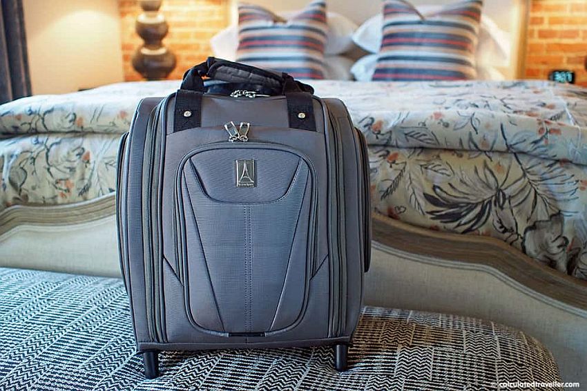 A small square suitcase with wheels and pockets on both sides and the front.