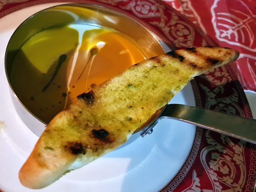 A small saucepan seen from above, with a brownish liquid in it - with streaks of sour cream - and a long piece of toasted and buttered bread balanced across it.