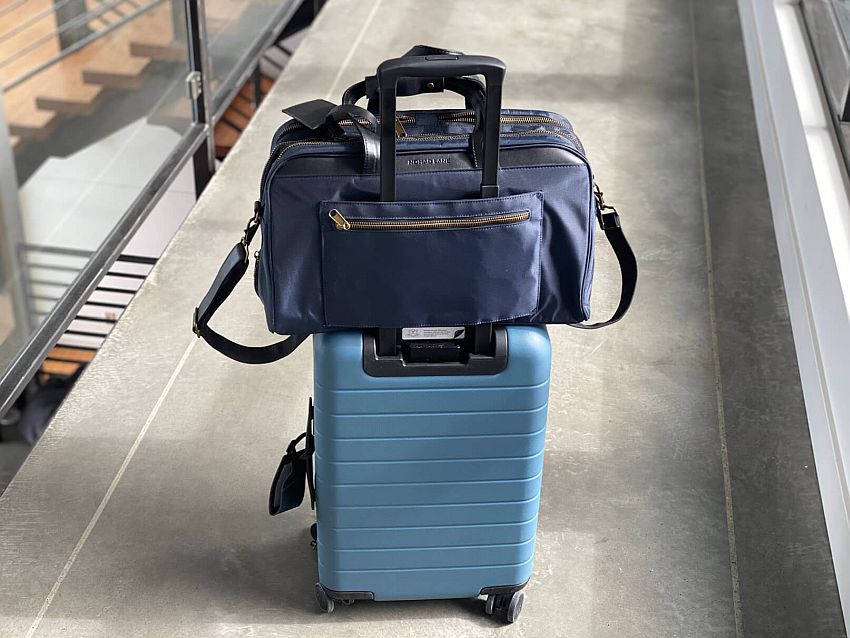 Minimalist packing tips: This should be enough: Two bags, one sitting on top of the other. The bottom one is a blue, hard-sided wheeled bag. The one on top is a thick-ish laptop case with a shoulder strap hanging down.