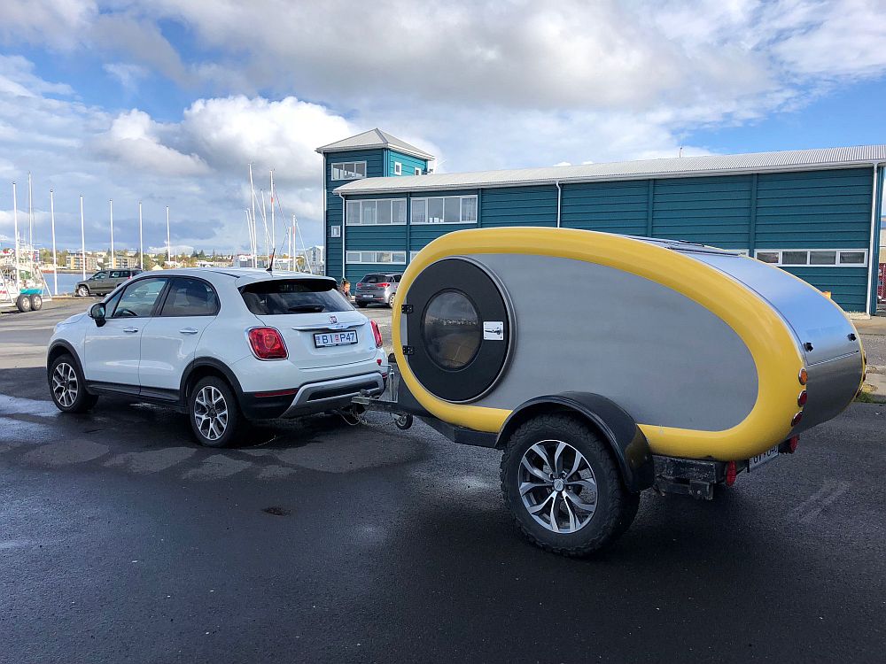 A small white 4x4 with a teardrop-shaped camping trailer hitched behind it.