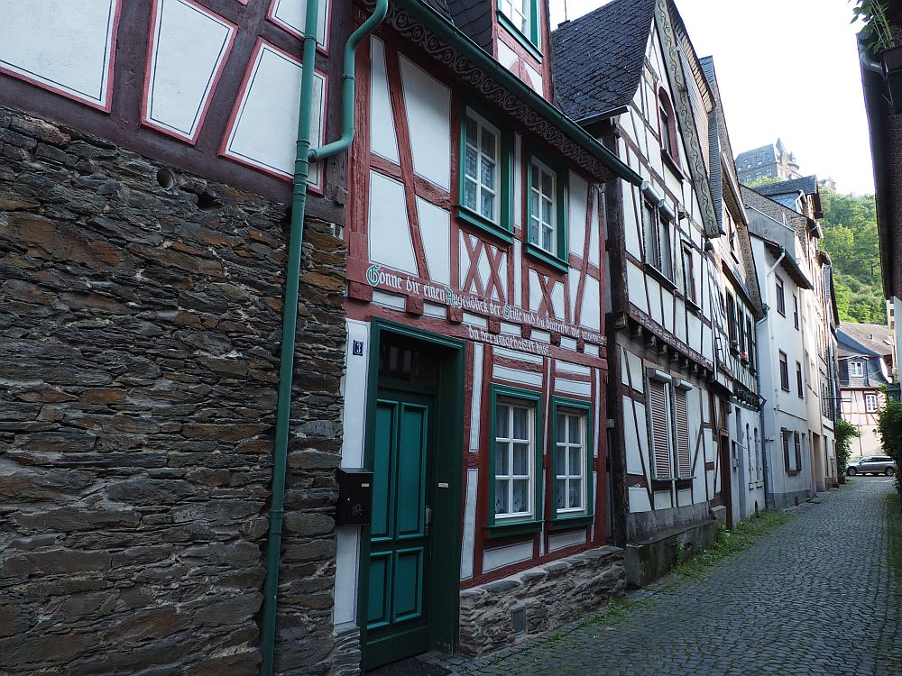 Looking down a narrow road in Bacharach Germany, primarily looking down one side of the road, which is lined with 3-story houses with half-timbered exteriors. The timbers are brown, the walls between the timber are white plaster.