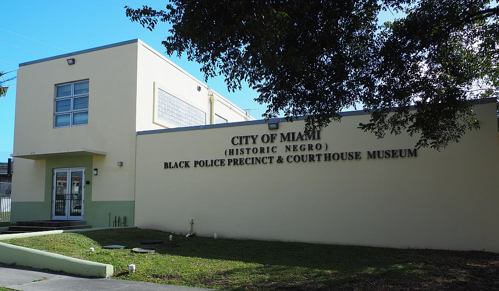 A plain beige facade, two stories on the left, one story on the right. Letters on the side read "City of Miami (Historic Negro) Black Police Precinct & Courthouse Museum"