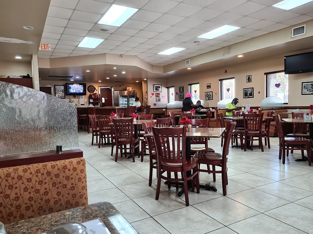 A big, brightly lit room, with booths along the two sides and square tables in two rows down the middle. IN the back, a counter with a tv hanging above it.