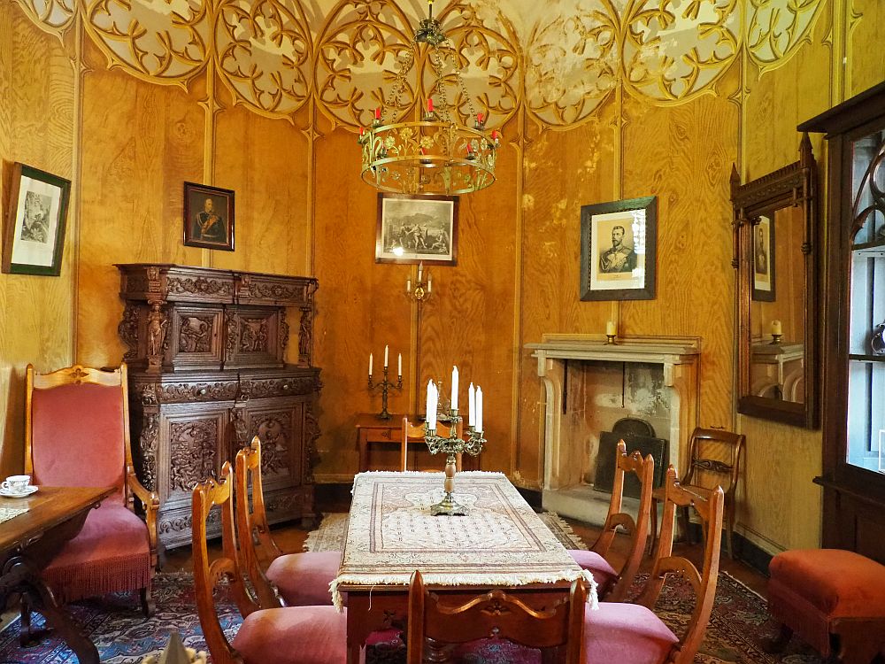 A table in the center with a simple candelabra standing on it and five chairs around it. An ornate carved chest at the back wall left and a fireplace at the back wall right. The wall, by the way, is curved to an oval shape. The wall is painted in a trompe l'oeil, so it looks as if there are gothic filigrees all around the top of the wall. 