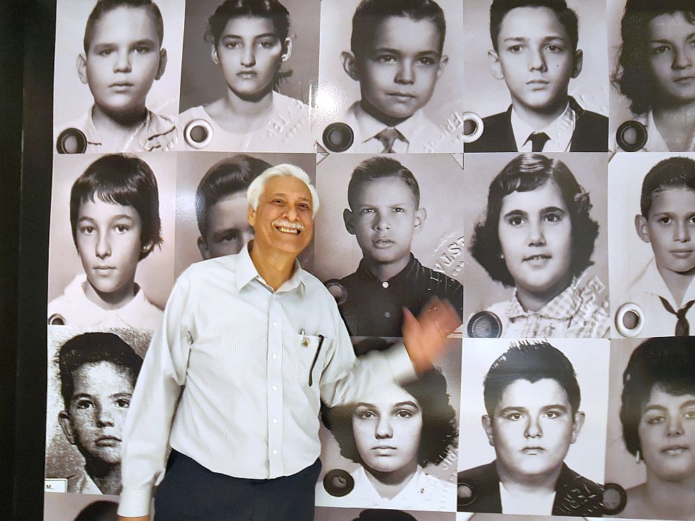 Mr. Llores stands in front of a wall of large black and white photos of children. He waves his hand and smiles next to the photo of himself as a child. The Pedro Pans are part of the history of Little Havana.