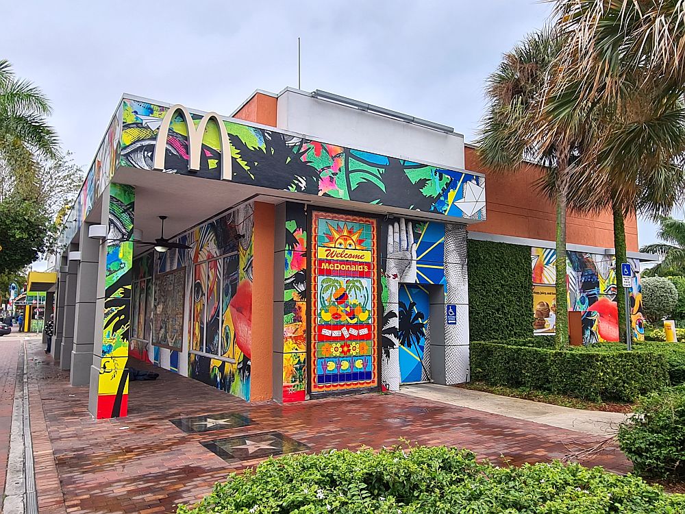 The single-story building has a collage of murals on it: an eye is visible, and a hand, and tropical foliage. 