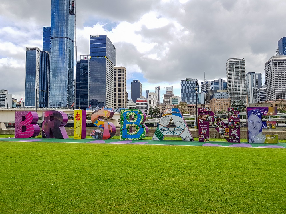 View of Brisbane city. Foreground: brightly painted letters spell out the word "Brisbane". Behind, lots of tall buildings of various shapes and sizes.