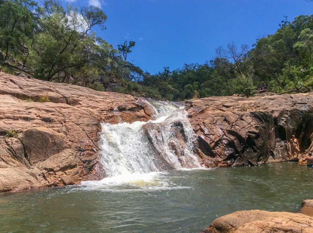 A wall of rock on the far edge of a pool. A small waterfall falls over the edge of the rock into the pool.
