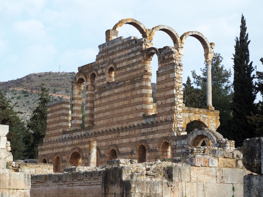 Walls of a building showing arches over the doorways: the wall is made of rows of white stone alternating with rows of reddish bricks.