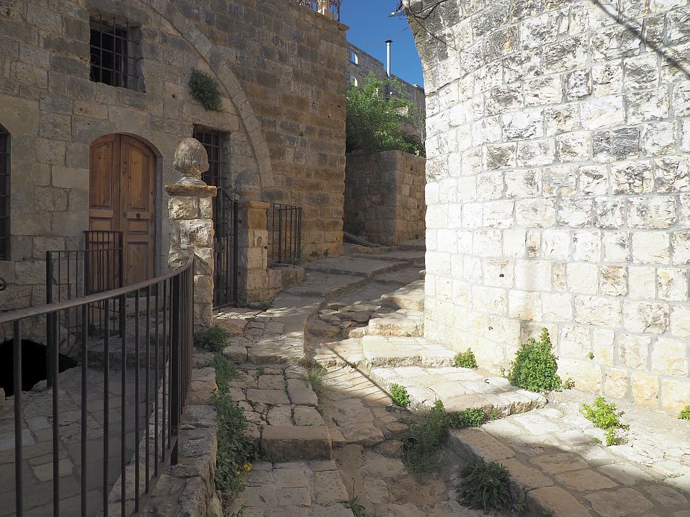 A road curving up a small hill. On the right, a stone wall, on the left a small house with an arched front. The road has a gutter down the middle and stairs on both sides of the gutter, all built of stone blocks.
Lebanon Travel tips