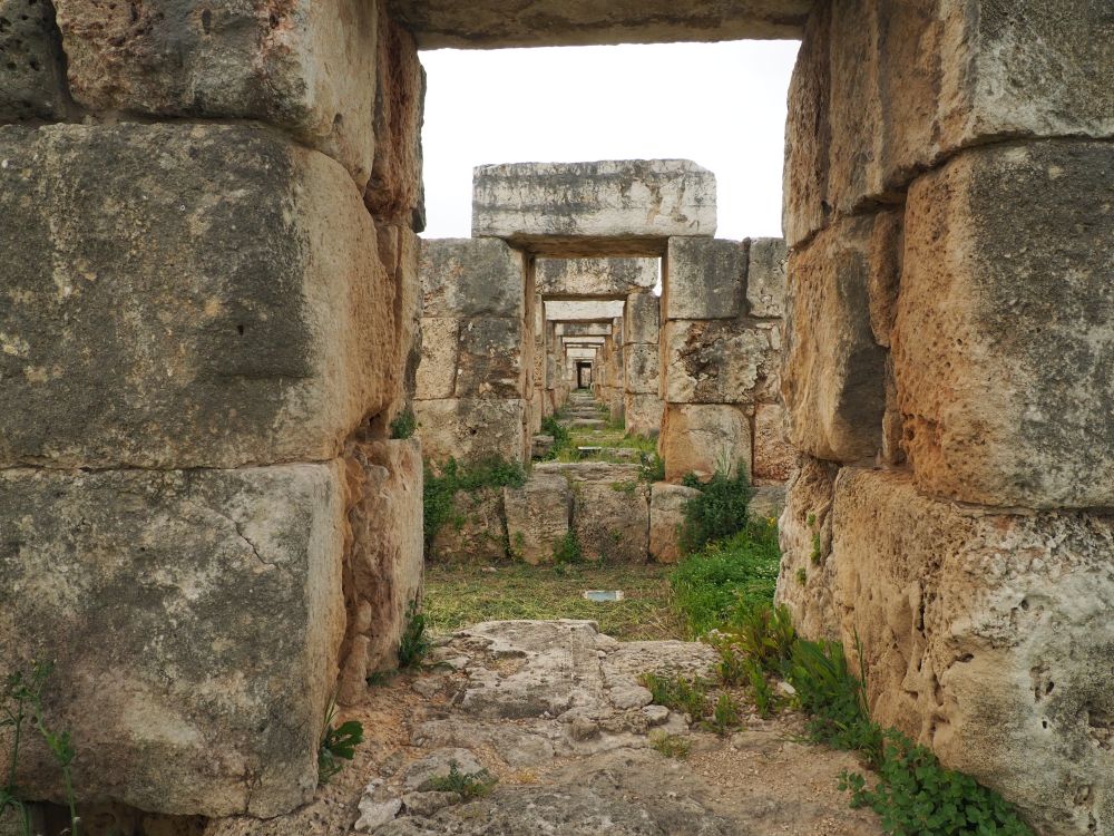 Sighting down a long tunnel of structures: large stones piled on either side, a bigger stone across the top of each doorway.