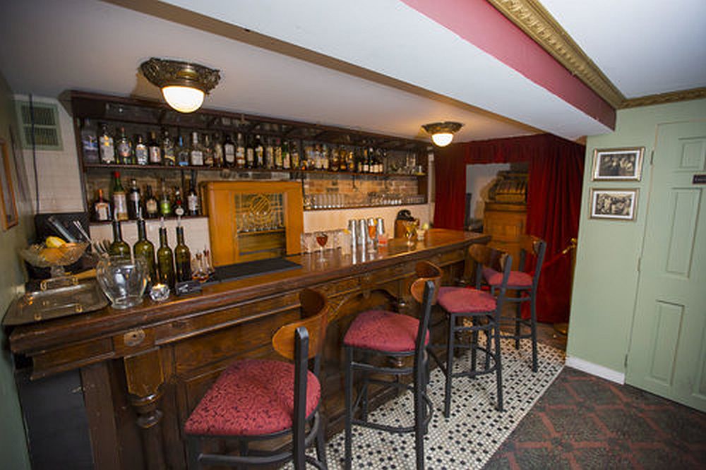 The bar, wood with a row of bar stools, shelves with bottles, and a vintage radio mounted behind the bar.