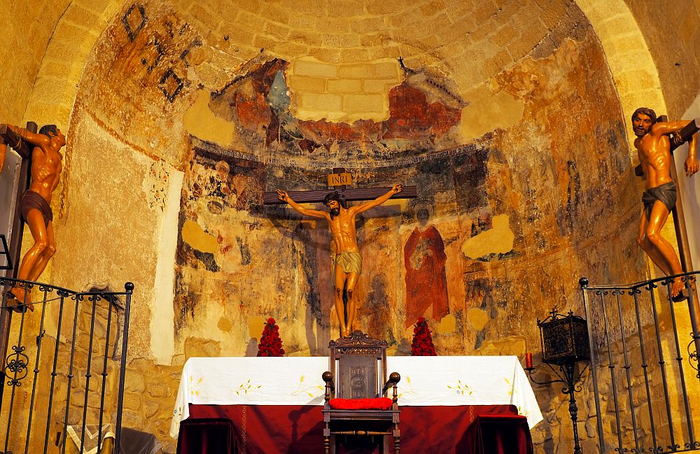 A Romanesque half-dome behind the altar. On the altar a figure of Jesus on the cross and the two crucified thieves on either side. The back wall has the remains of frescos.