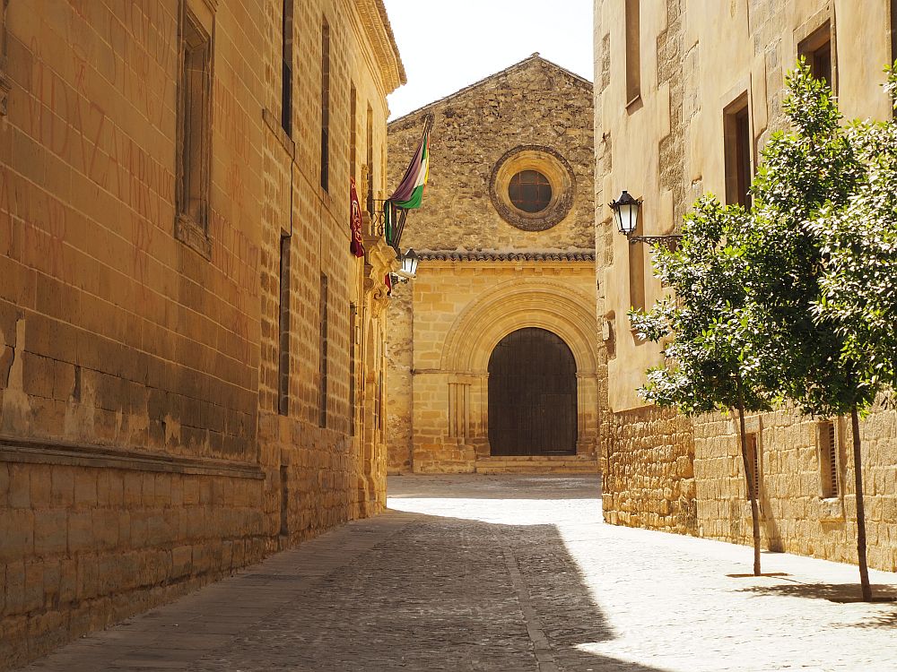 Looking down a cobbled road between stone sides of two buildings, the church is visible at the end of the road: a Romanesque arched entrance with a round window above it.