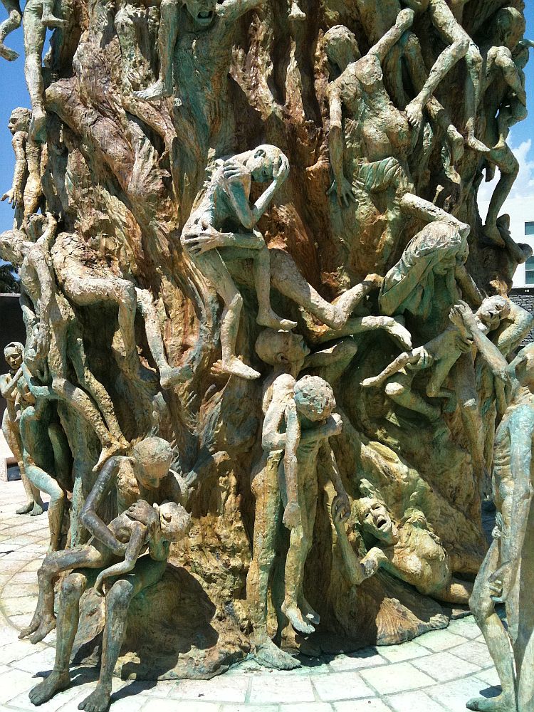 At the base of the giant arm statue at the Miami Holocaust Memorial: the arm is covered with figures of people. Some are holding children, some are trying to climb up, all have faces of anguish.