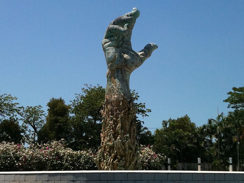 A phot of the arm statue at the Holocaust Memorial in Miami. It is an forearm reaching up toward the sky. While the wrist and hand look like a normal write and hand, the lower part is bumpy with images of humans.