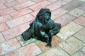 A statue of a child siting on the ground, looking up and crying as she reaches her hand out for help. Miami Holocaust Memorial.