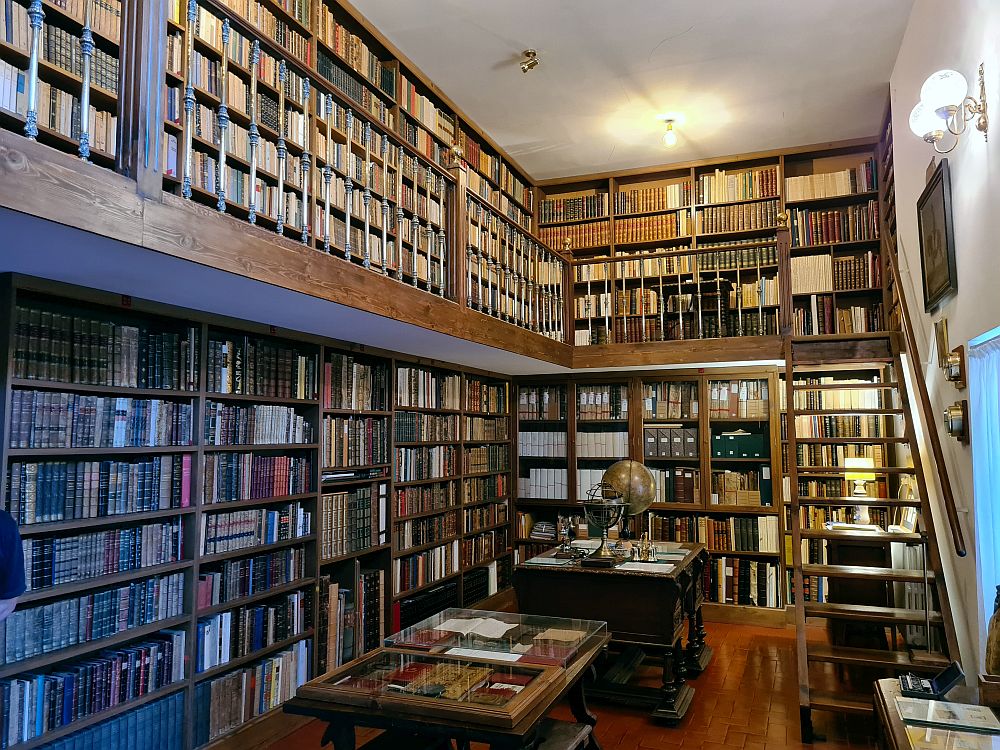 A not very large two-story room, with a balcony along two of the sides and a stairway allowing access to the books on the upper story. The entire two walls are coved with shelves filled entirely with books.