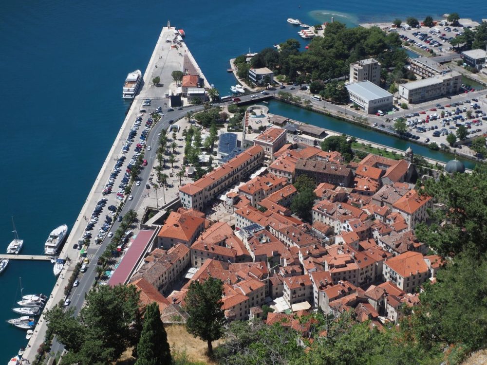 The Old City of Kotor is a tight cluster of buildings with red tile roofs, the sea on the left and a river edging it on the right.