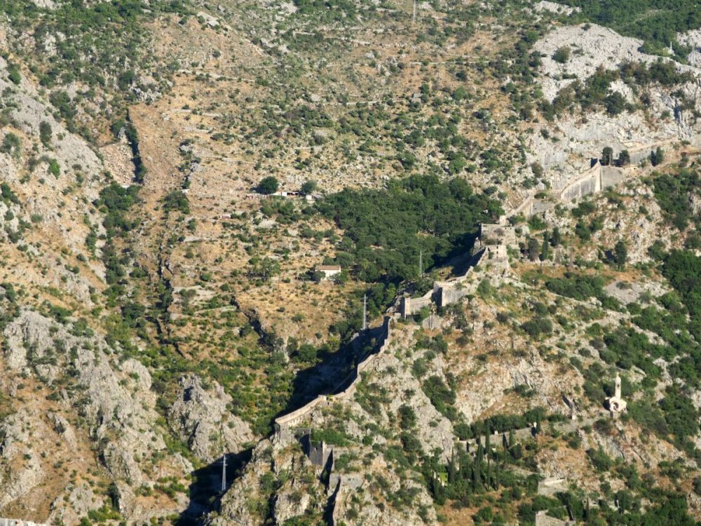 The wall follows a ridge on the stony side of a mountain up to the ruined buildings that are the remains of San Giovanni Fortress.