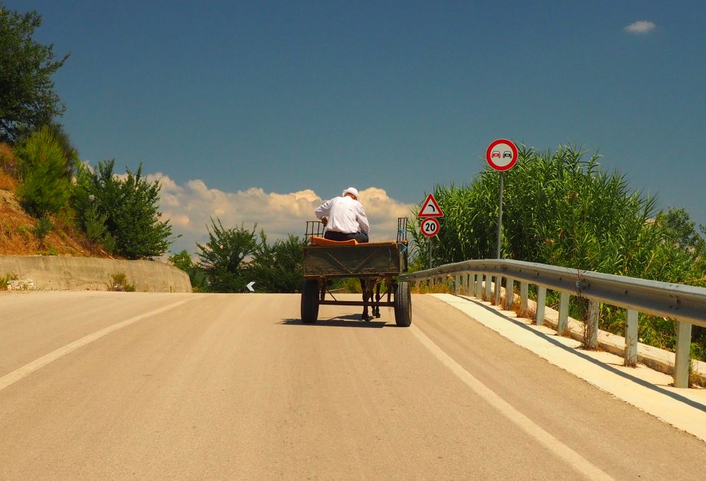 Image of a paved road with a horse and wagon, as seen from behind.