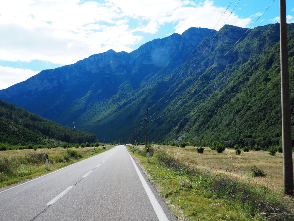 Straight paved road ahead into the distance, very steep craggy mountains ahead. Albania travel tips.