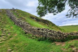 A section of Hadrian's wall, in neat rows of cut stone, climbs a gentle hill surrounded by grassy fields.