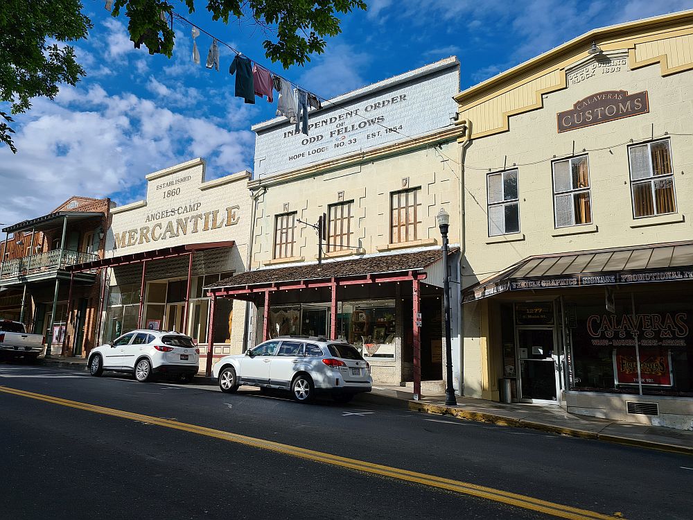 A row of Gold-Rush-era buildings: each has a shaded sidewalk in front of it and some level of false front. 