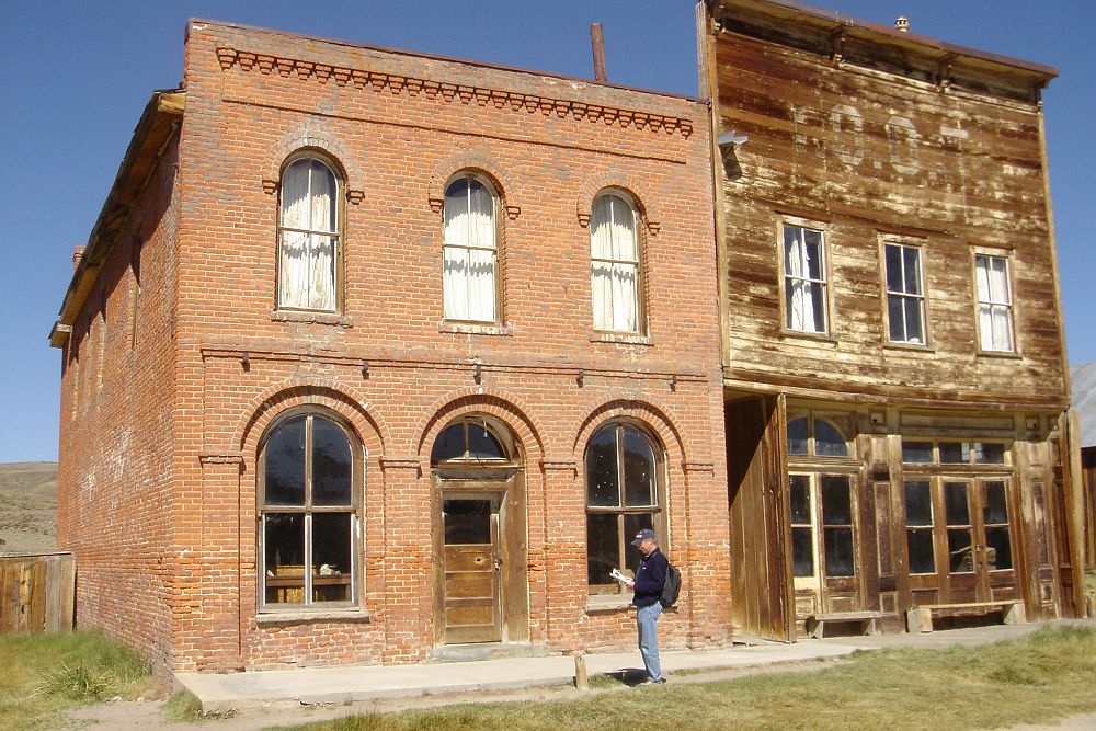 Two buildings in Bodie, ghost town in California: left, a brick building, 2 stories, with arched windows and door; right, a wooden building, also 2 stories but with a tall false front.