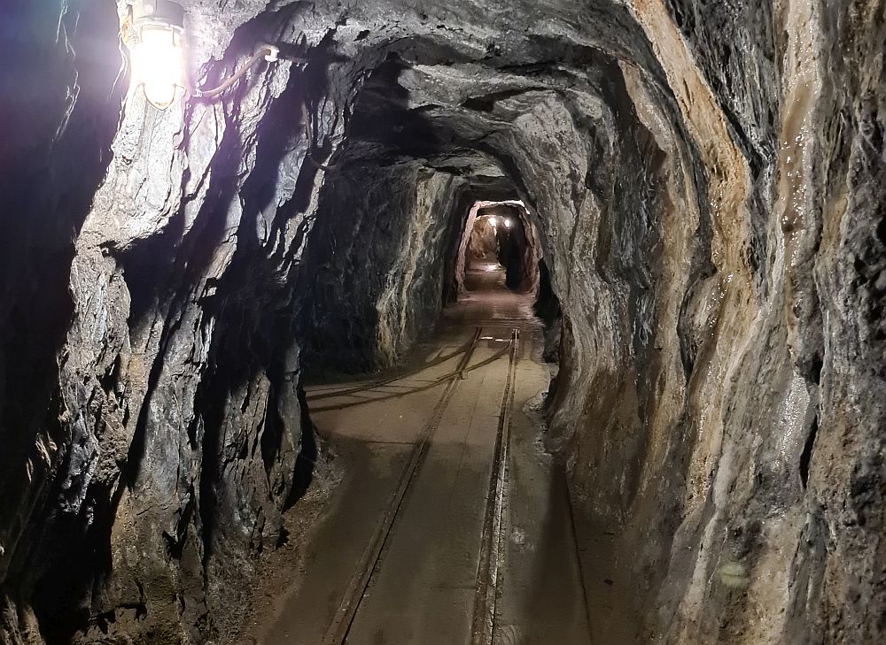 A tunnel straight ahead, carved out of rock so the walls are uneven of gray stone.