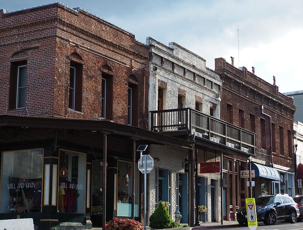 Two-storey brick buildings, each with a balcony shading the sidewalk.