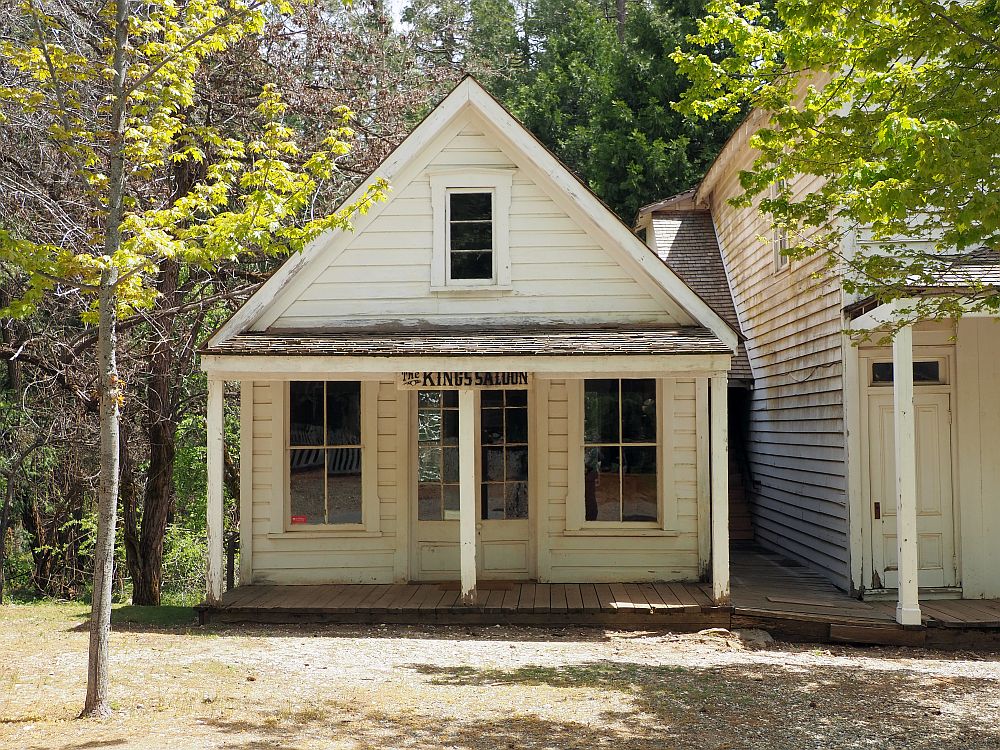 A simple little white house with a door in the middle, one window on either side of it, a front porch with a roof. One window in the peaked roof. A sign over the door reads "The King's Saloon". At North Bloomfield ghost town in California  