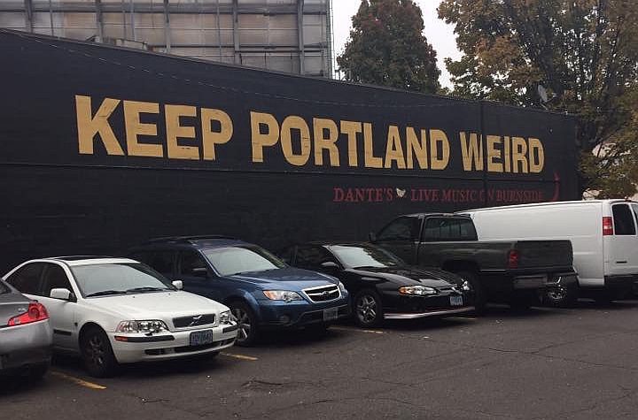 A wall with the words "Keep Portland Weird" painted across it. Cars parked in front of it.