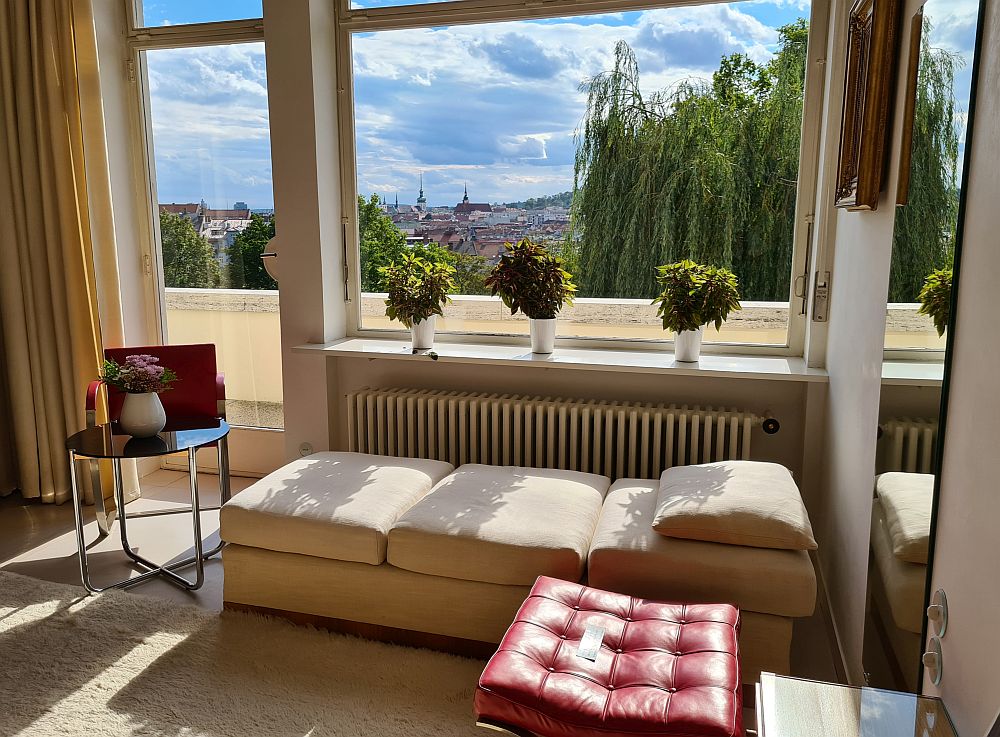 Looking toward the window and the glass door next to it: a chaise longue under the window, a design chair and table next to that, and a red upholstered design stool too.