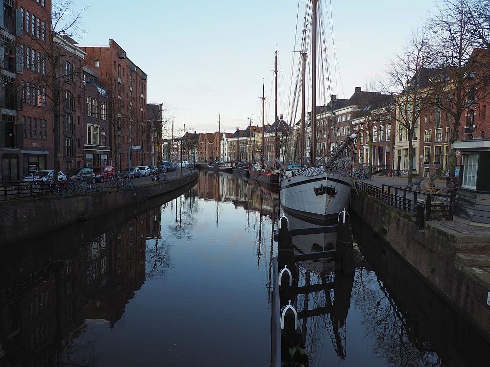 A canal extends ahead, curving gradually to the left. Very still water. Old ships line the right side. Next to them, a row of ex-warehouses, now houses and apartments.