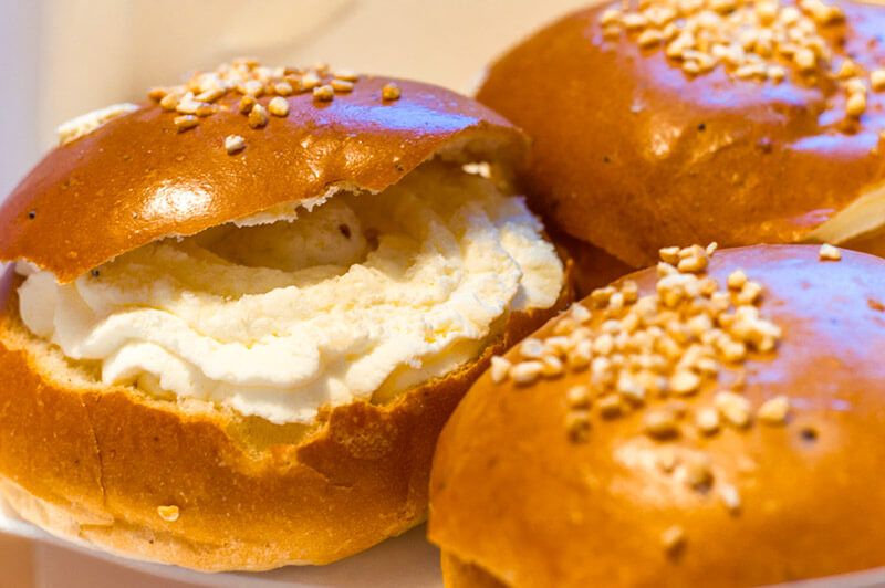 Round rolls sliced open, with white cream between top and bottom and a sprinkling of chopped nuts on top.