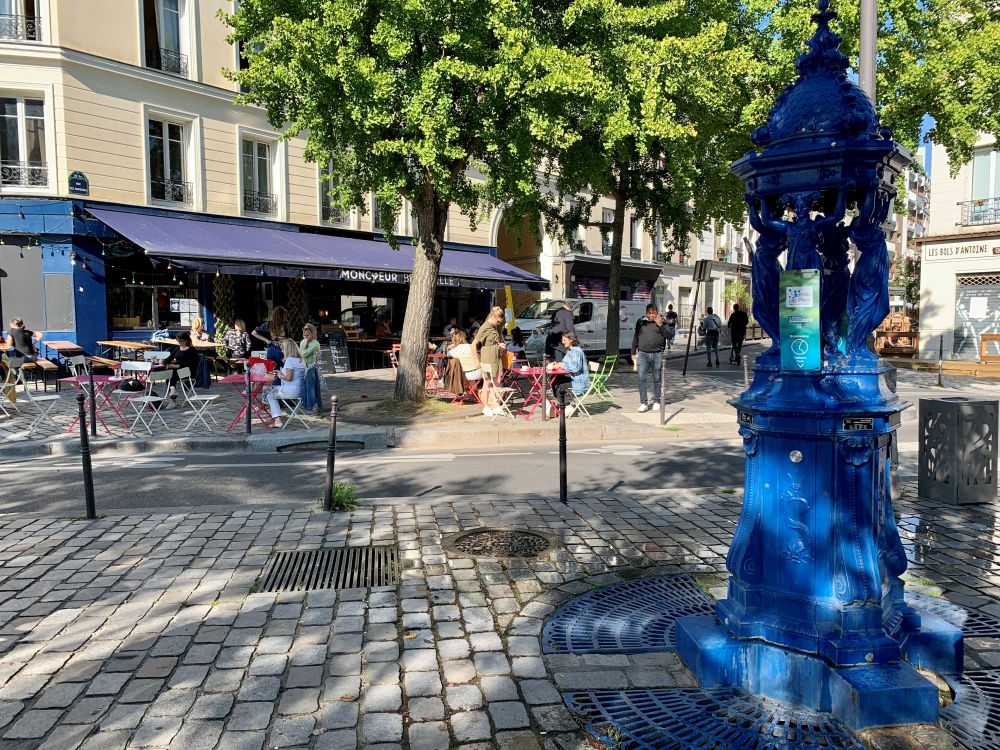 A square with a sidewalk cafe and a tall iron fountain, painted bright blue.