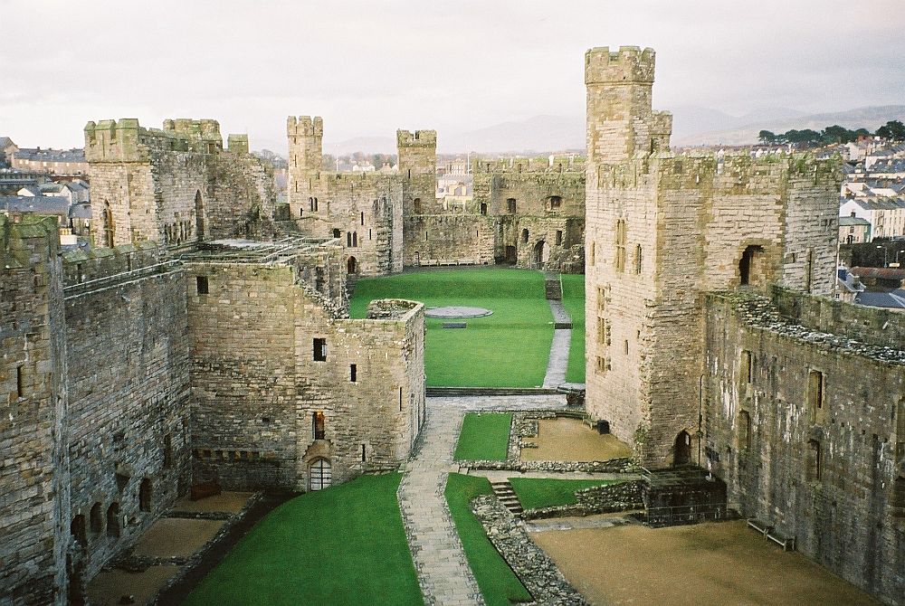 Looking down on a very large castle, only it's outer walls remaining. Crenellated along the tops, with towers at each corner, and grassy area inside.